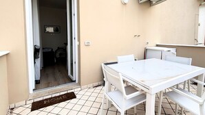 Una habitación con una mesa y sillas blancas, una puerta que da a un pasillo y un equipo de aire acondicionado instalado en la pared.