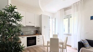 Una cocina moderna con armarios blancos, un comedor con mesa y sillas, y una sala de estar con sofá y cortinas.