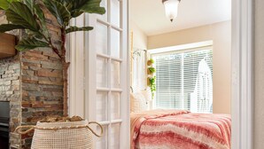Een slaapkamer met een houten vloer, een bed met een rood-wit gestreept dekbed, een witte deur, een hanglamp en een plant aan de linkerkant.