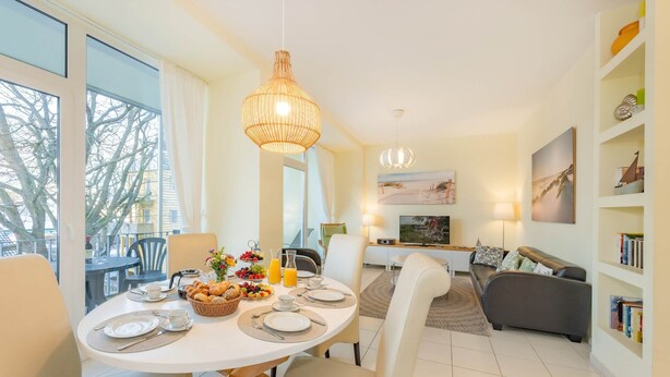 Ein modernes Wohnzimmer mit Essbereich, ausgestattet mit einem runden Frühstückstisch, einer Couch und einem Bücherregal.