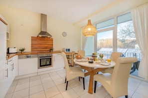 A modern kitchen with a central island, white cabinetry, a built-in oven, and a large window with curtains. - Südwind 13 - two bedrooms in a prime location, sauna, swimming pool and balcony (Zempin)
