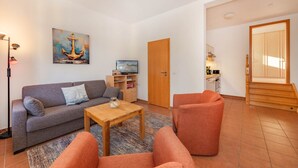 A living room with a sofa, armchairs, a coffee table, and a painting of an anchor. - Villa Kaiserhof 05: Stylish vacation apartment with balcony near the beach in Zinnowitz (Zinnowitz)