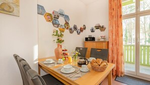 A dining area with a table set for breakfast, including plates, cups, and a fruit basket. - Villa Kaiserhof 05: Stylish vacation apartment with balcony near the beach in Zinnowitz (Zinnowitz)