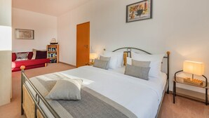 A neatly arranged bedroom with a large bed, bedside tables, a red sofa, and a bookshelf. - Villa Kaiserhof 05: Stylish vacation apartment with balcony near the beach in Zinnowitz (Zinnowitz)