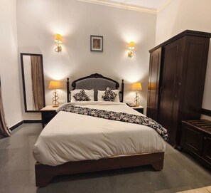 A neatly made bed with a patterned bedspread, two bedside lamps, a framed picture above the bed, and a dark wooden wardrobe to the right.