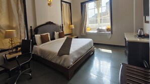 Une chambre d’hôtel avec un lit, des tables de chevet, un bureau, une chaise et une fenêtre avec des rideaux.