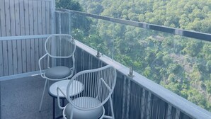 Un balcon avec deux chaises blanches et une vue sur une colline boisée.