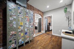 Een gang met een bakstenen muur, houten vloer en een metalen kast beplakt met stickers.