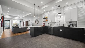 Une cuisine moderne avec des meubles de couleur sombre, un grand îlot central et des luminaires suspendus.