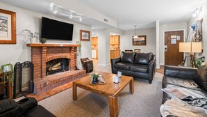 Una sala de estar con chimenea, sofás de cuero, una mesa de centro y un televisor montado en la pared.