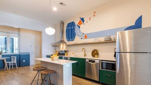 Una cocina moderna con una isla central, armarios verdes, electrodomésticos de acero inoxidable y un mural decorativo.