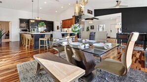 A modern kitchen with dark cabinets, a central island, and a dining area with a glass table and wooden chairs. - Waterfront, Infinity Pool, Dock, Outdoor Bar, Beach Access | Riverside Veranda (Fort Lauderdale)