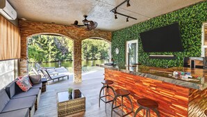 A modern outdoor bar area with a wooden counter, bar stools, and a seating area with a sofa and chairs. - Waterfront, Infinity Pool, Dock, Outdoor Bar, Beach Access | Riverside Veranda (Fort Lauderdale)
