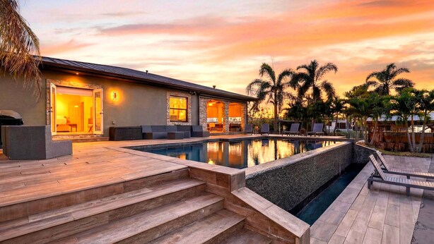 A poolside area with a wooden deck, steps leading to a house, and palm trees. - Waterfront, Infinity Pool, Dock, Outdoor Bar, Beach Access | Riverside Veranda (Fort Lauderdale)
