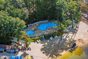 An aerial view of a resort with two swimming pools surrounded by lounge chairs and umbrellas, a sandy beach area, and a small building with a flag. - Lake Harmony Home • Loft + Game Room • Near Lake + Ski | Mountain Laurel Lodge (Lake Harmony)