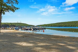 A lakeside dock with boats, a sandy beach, and forested hills in the background. - Lake Harmony Home • Loft + Game Room • Near Lake + Ski | Mountain Laurel Lodge (Lake Harmony)