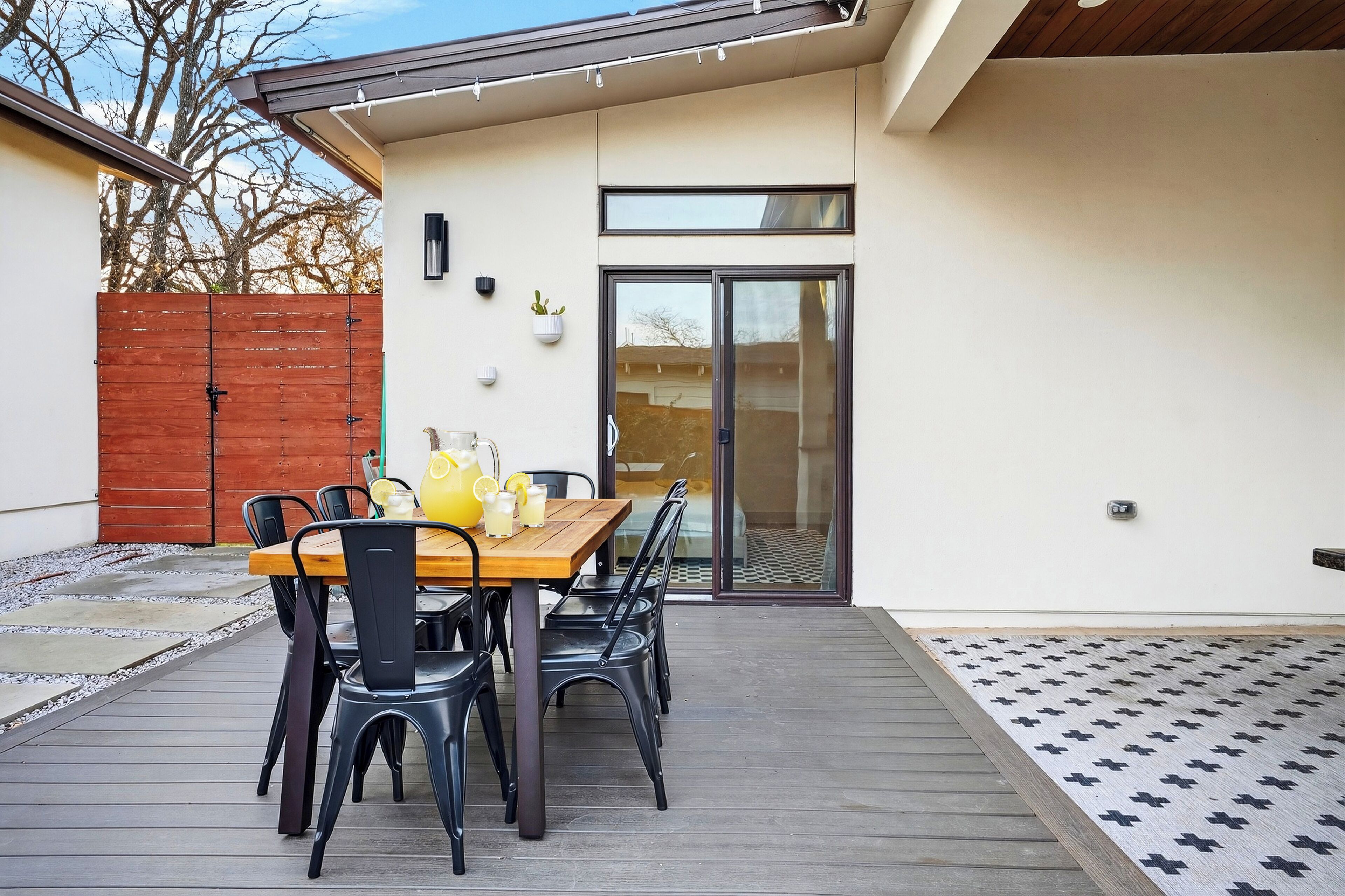 A patio with a wooden table and chairs, a yellow pitcher, and a glass of lemonade.