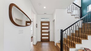 Ein Flur mit Holzdielen, einer Holztür, einer Treppe mit schwarzen Geländern und einem Spiegel an der Wand.