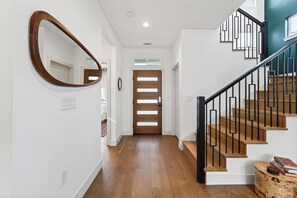 A hallway with wooden flooring, a wooden door, a staircase with black railings, and a mirror on the wall. - Modern East Austin Retrest + Movie Room + Outdoor Kitchen + Near Downtown (Austin)