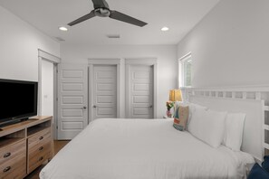 A bedroom with a bed, a TV on a wooden dresser, a ceiling fan, and two white doors. - Sleeps 16 | Mins to Miramar Beach + Community Pool | Sea Love by AvantStay (Miramar Beach)