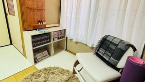 Une pièce chaleureuse avec une armoire en bois, une bibliothèque remplie de livres, un tapis moelleux, un fauteuil avec un coussin et une fenêtre ornée de rideaux légers.