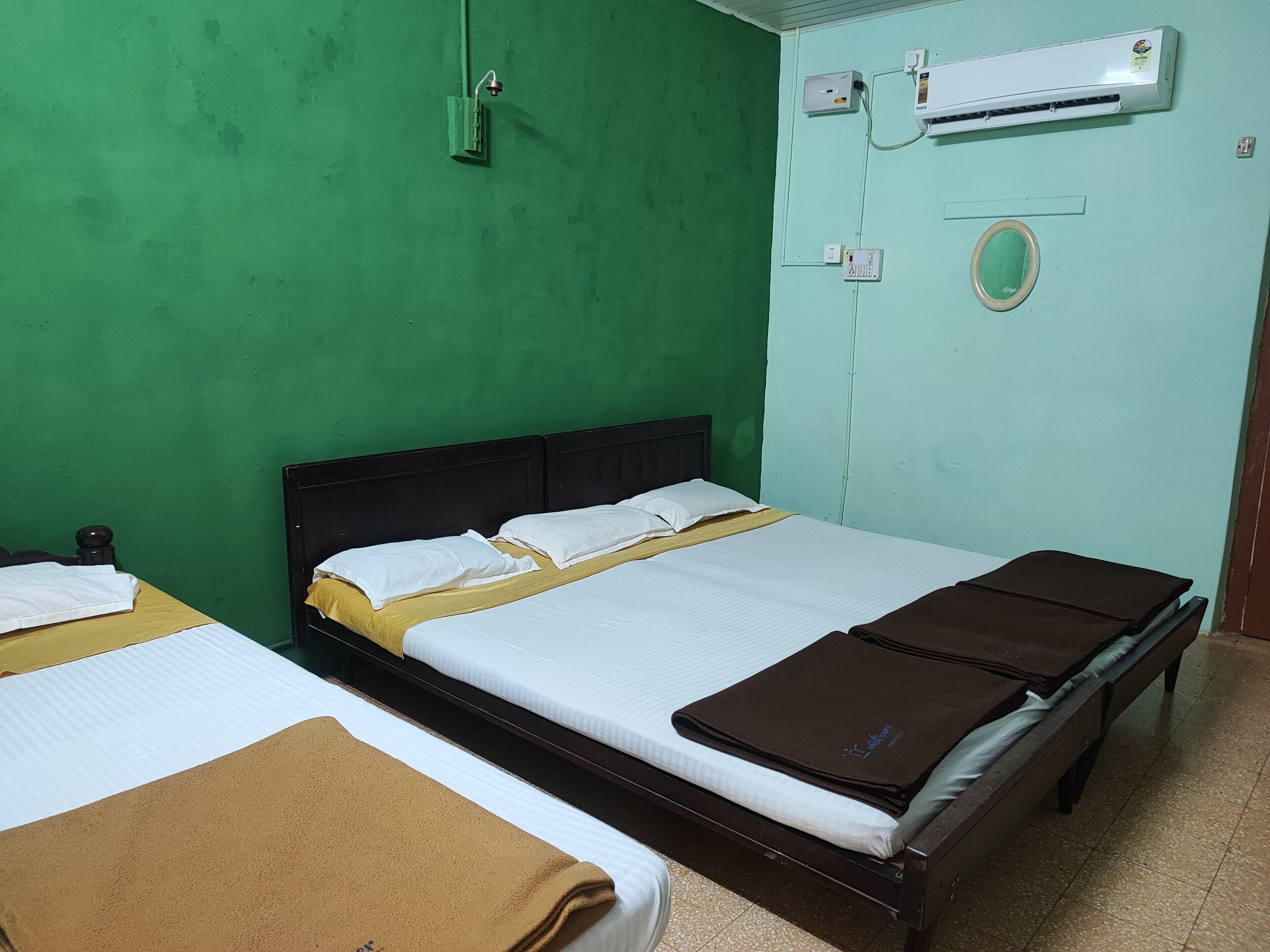 A room with two beds, a green wall, an air conditioning unit, and a power outlet.