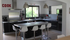 Una cucina moderna con isola centrale, sgabelli da bar, elettrodomestici in acciaio inossidabile e illuminazione a sospensione.