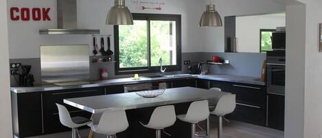 A modern kitchen with a central island, bar stools, stainless steel appliances, and pendant lighting.