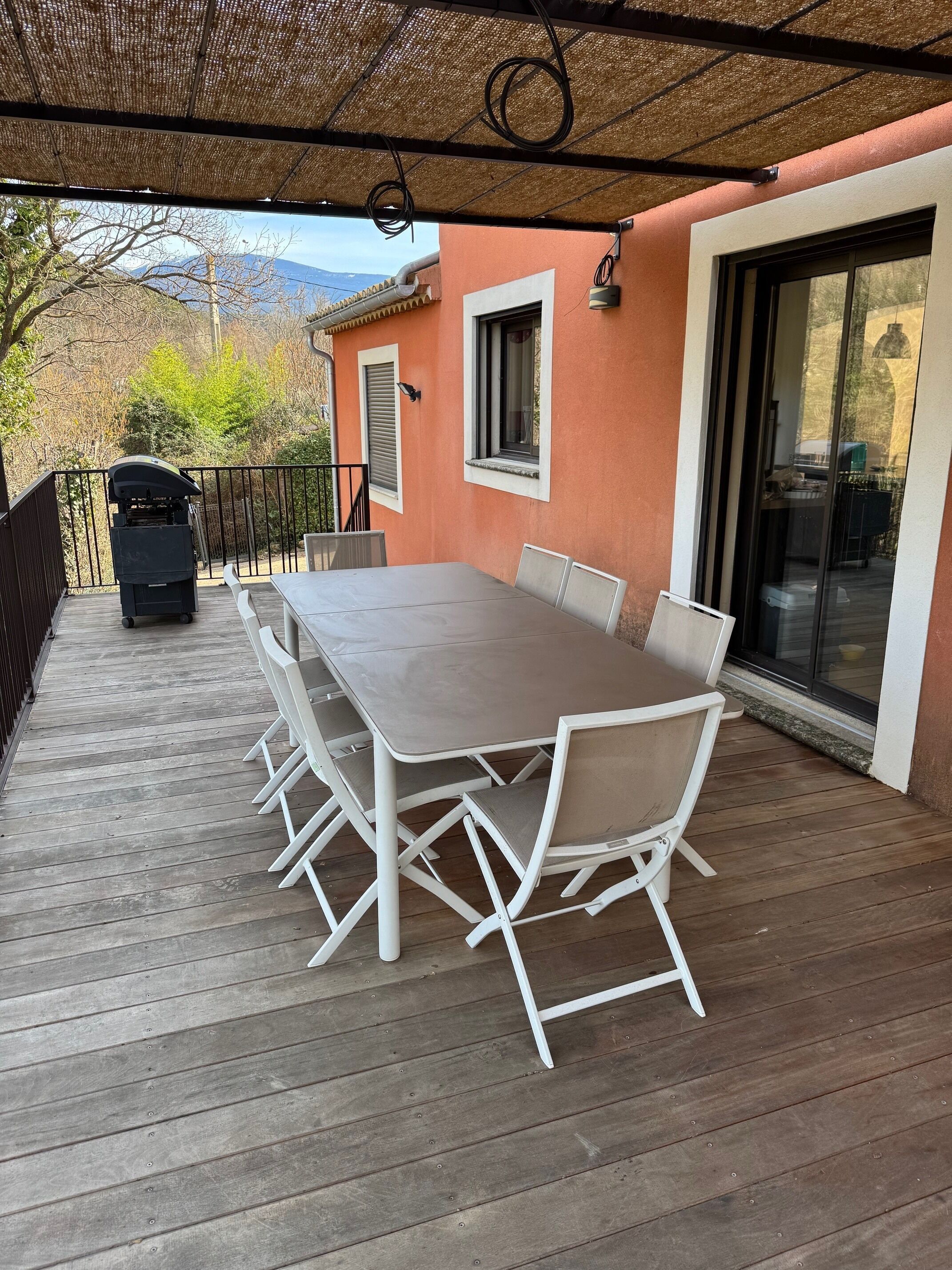 Una veranda riparata con pavimento in legno, un tavolo con sedie, un barbecue e una porta scorrevole in vetro.