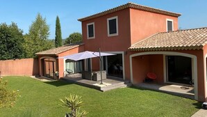 Una casa a due piani con tetto in tegole, un portico coperto con mobili da esterno e un prato curato.