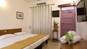 Une chambre d’hôtel avec deux lits, une tête de lit en bois, une plante en pot, une porte violette et une petite table avec des serviettes.