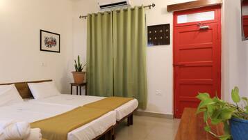 Habitación de hotel con cama, puerta roja, cortina verde, planta en maceta y un cuadro en la pared.