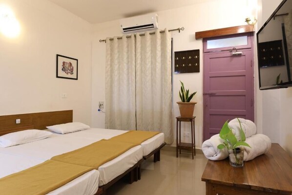 A hotel room with a bed, a small table with a plant, a purple door, and an air conditioning unit. - TELES WESTEND HOTEL (Vasco da Gama)