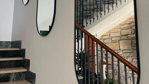 Un escalier avec un mur en pierre en arrière-plan, une main courante en bois et une rampe en métal. Il y a trois miroirs sur le mur.