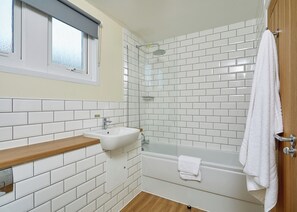 Une salle de bain avec des murs carrelés de carreaux blancs, un meuble-lavabo en bois, un lavabo, une douche et une baignoire.