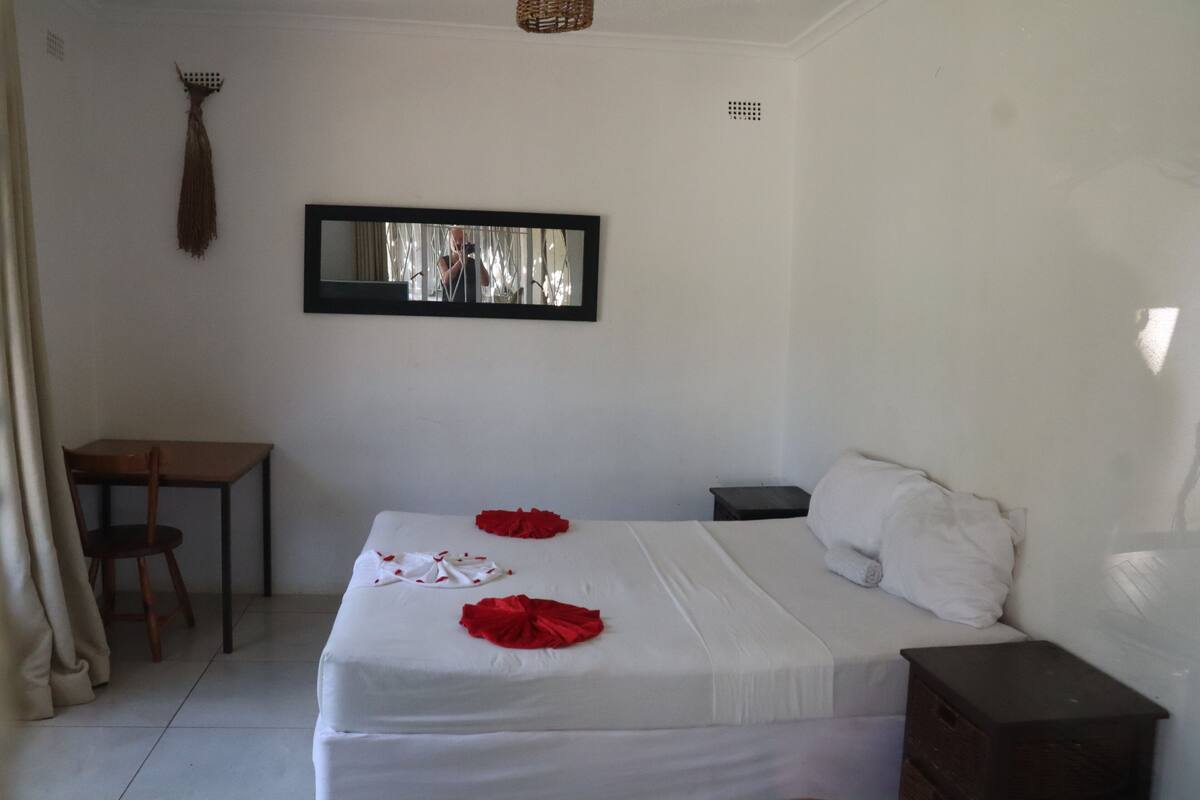 Habitación de hotel con cama, escritorio, silla, mesita y espejo en la pared.