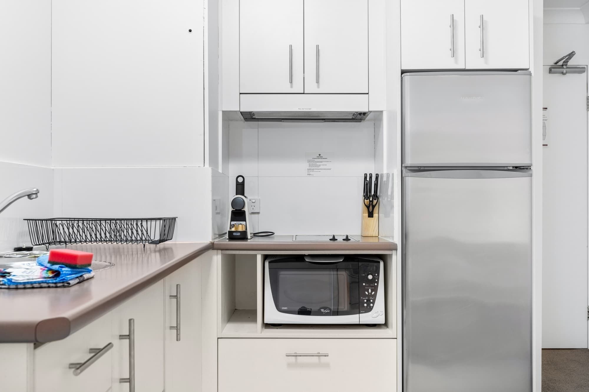 A compact kitchen with white cabinets, a built-in microwave, a coffee maker, and a knife block.