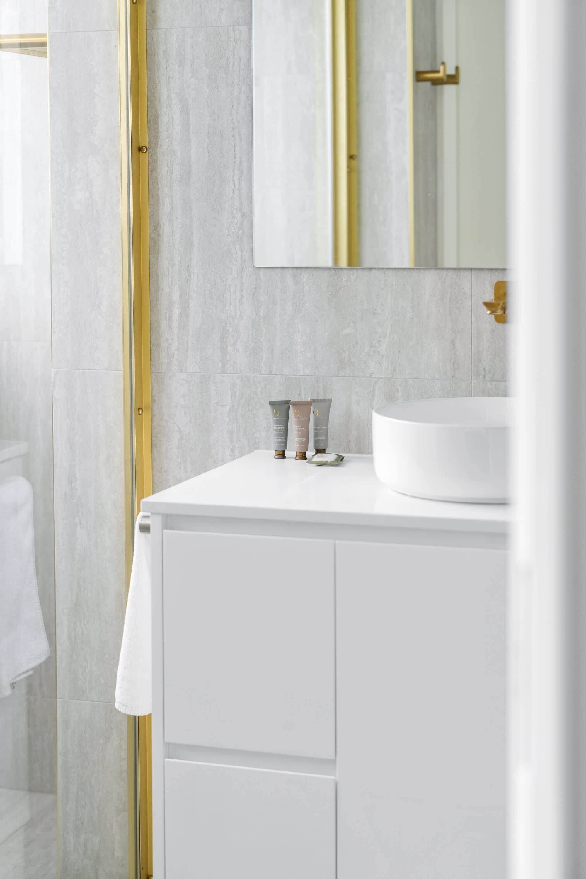 Ein Badezimmer mit einem weißen Waschbecken, goldenen Armaturen und einem Spiegel.