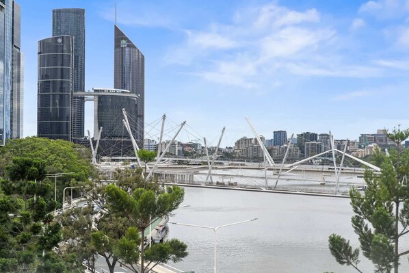 Un paysage urbain avec des gratte-ciel modernes, un pont aux câbles blancs et une étendue d’eau.
