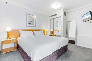 Une chambre d’hôtel avec un grand lit, deux tables de chevet avec des lampes, une armoire, un miroir et des œuvres d’art encadrées accrochées aux murs.