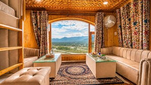 A room with a wooden ceiling, a sofa, a glass table, and a view of a landscape through a large window. - SRICHAN RESORTS (Pahalgam)