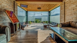 A modern interior with a high ceiling, a view of mountains, and a seating area with leather sofas and a glass table. - SRICHAN RESORTS (Pahalgam)