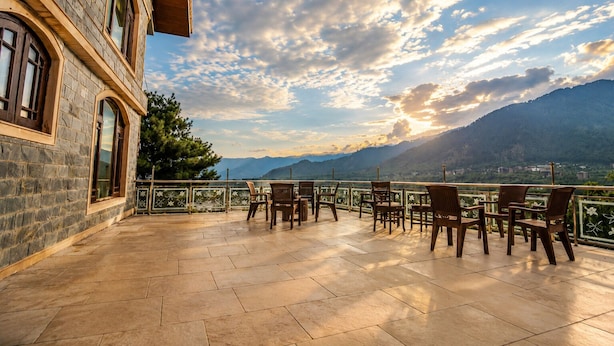A terrace with stone walls, a view of mountains, and outdoor seating. - SRICHAN RESORTS (Pahalgam)