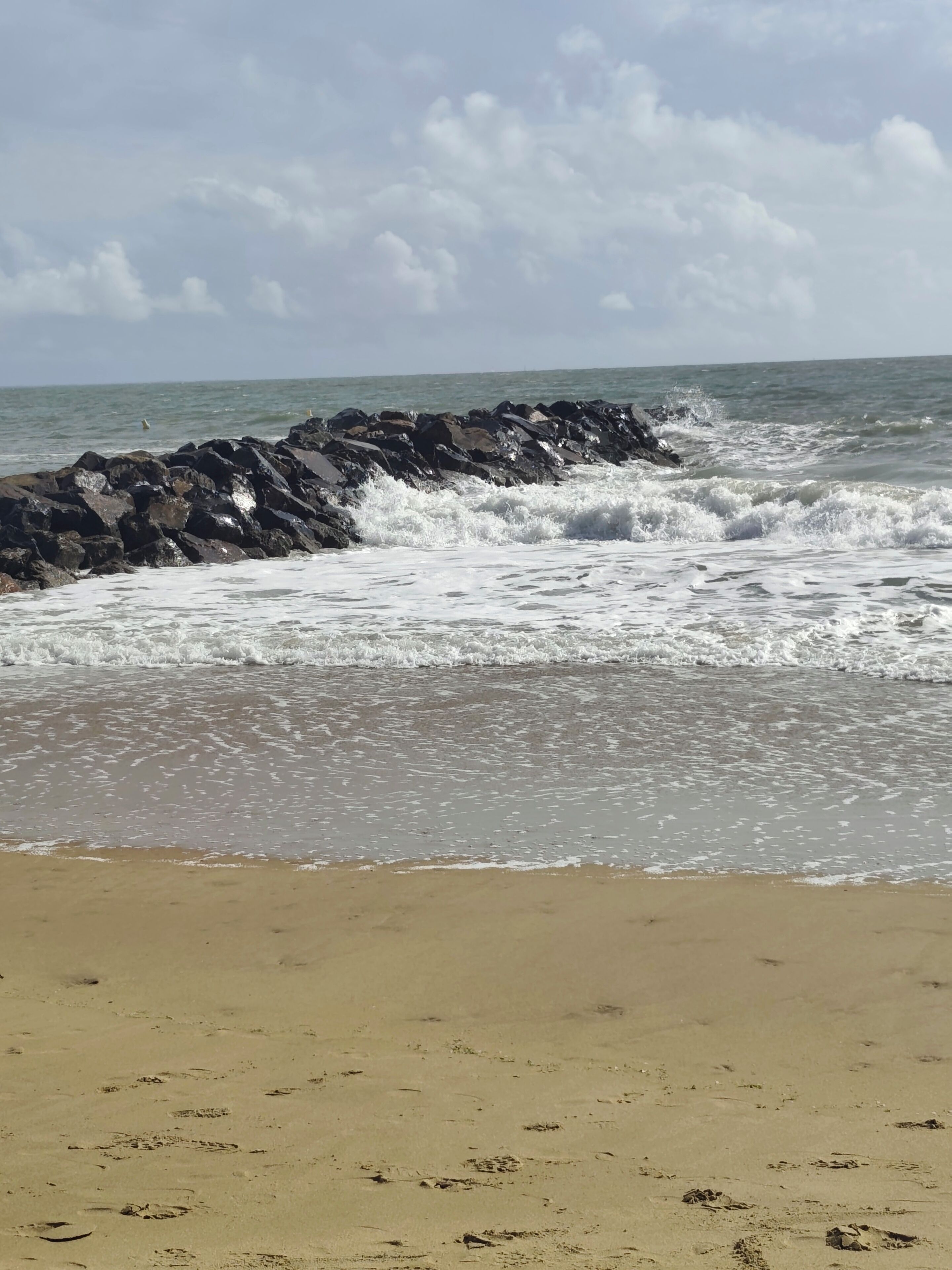 A beach with waves crashing against rocks and a sandy shore.