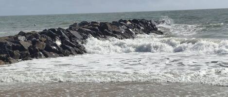 A beach with waves crashing against rocks and a sandy shore.
