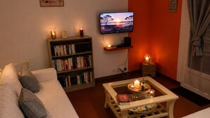 Ein Wohnzimmer mit einer Couch, einem Couchtisch mit Kerzen, einem Bücherregal, einem Fernseher und einer roten Wand.