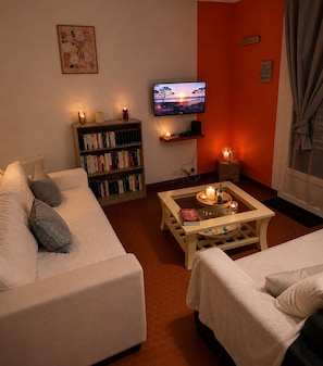 A living room with a sofa, a coffee table with candles, a bookshelf, a TV, and a red wall. - A vacation lulled by the sound of the sea! (Jard-sur-Mer)
