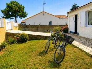 Ein Wohnhaus mit befestigter Auffahrt, ein weißes Haus mit Ziegeldach, einem Fahrrad und einem kleinen Garten mit Blumen und einem Baum.