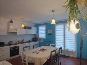 A kitchen with white cabinets, a dining table with chairs, and a hanging plant. - A vacation lulled by the sound of the sea! (Jard-sur-Mer)