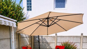 Eine Terrasse mit zwei roten Stühlen und einem grünen Liegestuhl unter einem großen Sonnenschirm.